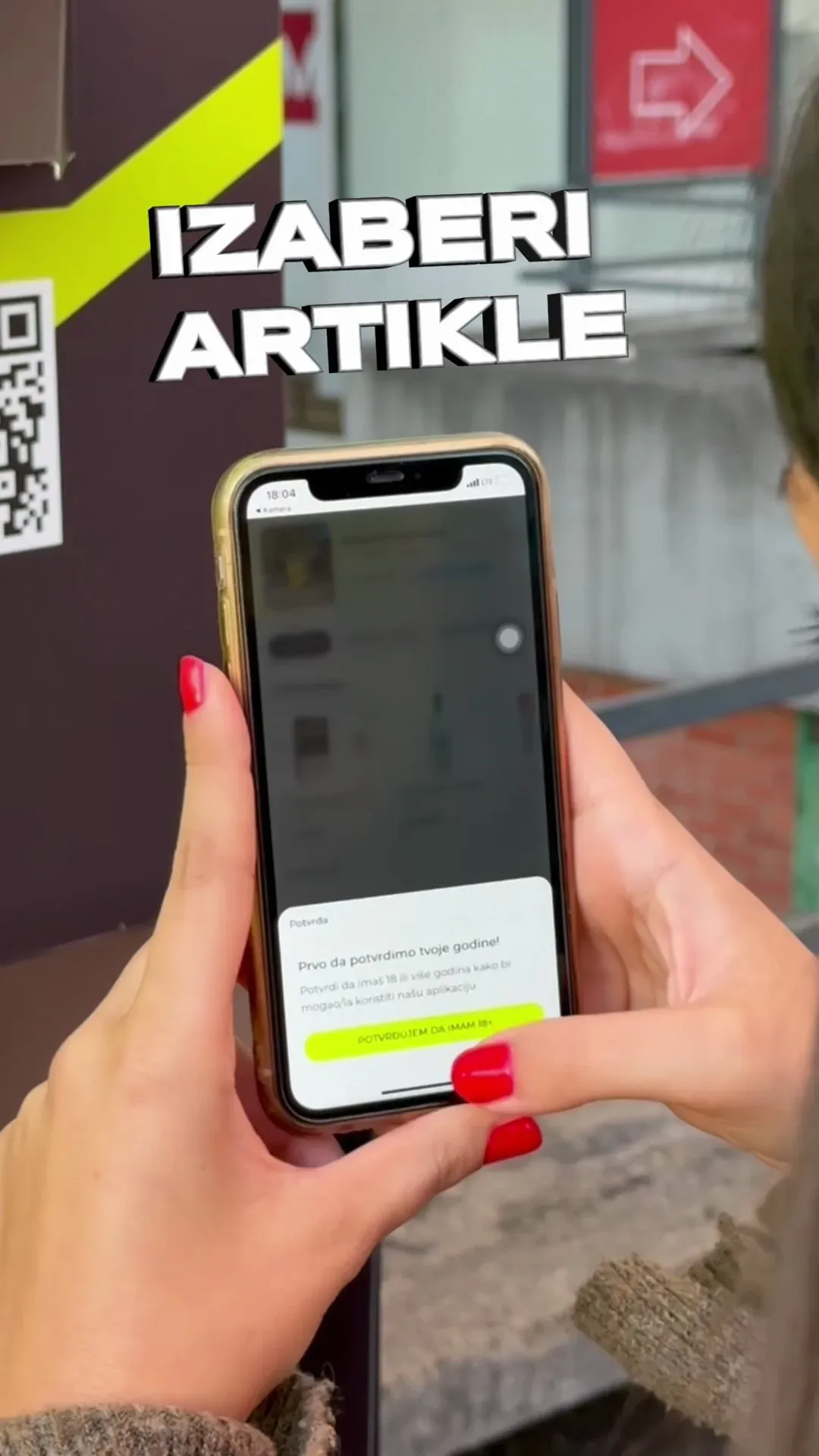 A hand holding a phone at a Kiosk24 kiosk, with the on-screen words 'Izaberi artikle' (choose items).